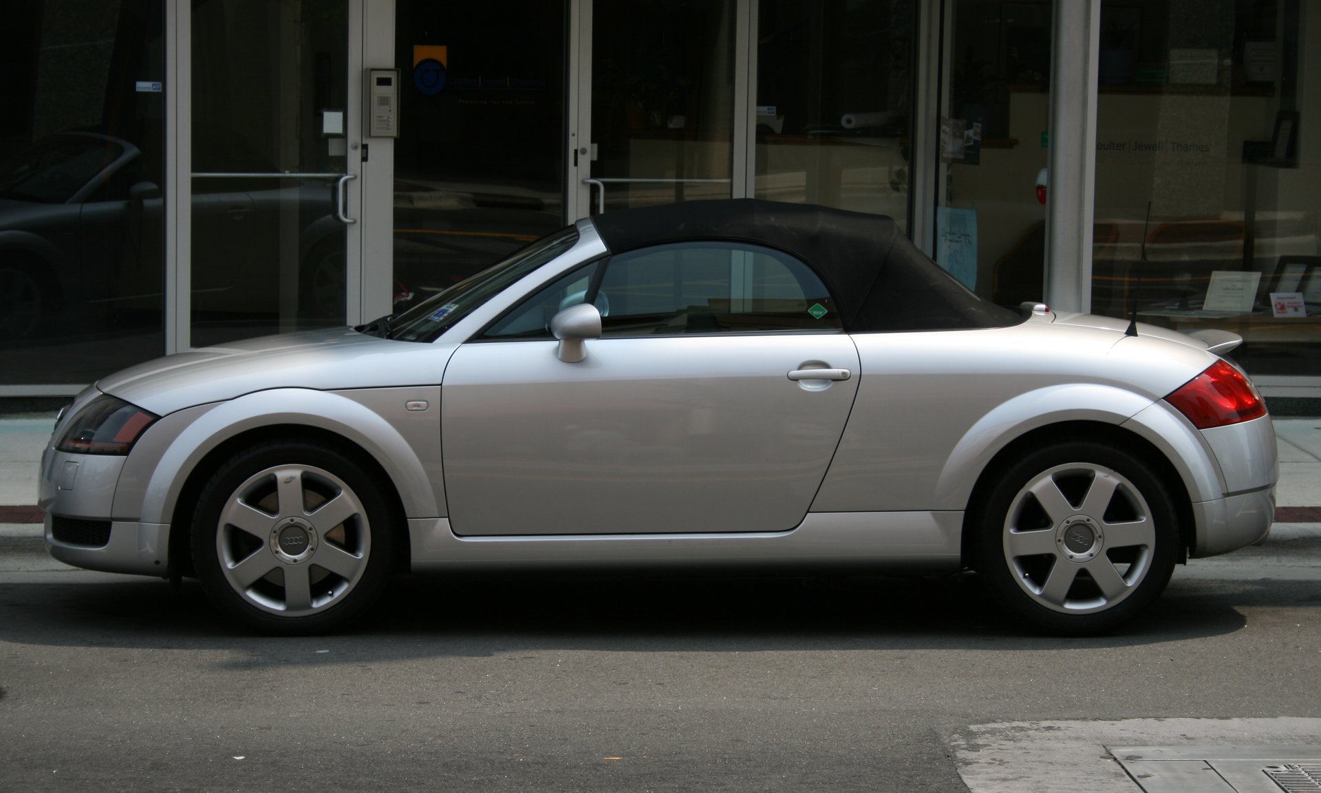 Side view of a silver first-generation Audi TT Roadster with its black fabric roof raised